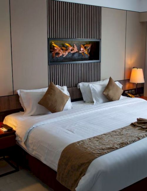 A hotel room features a king-size bed with pillows and lamps on nightstands, and a wall art piece decorates the space.