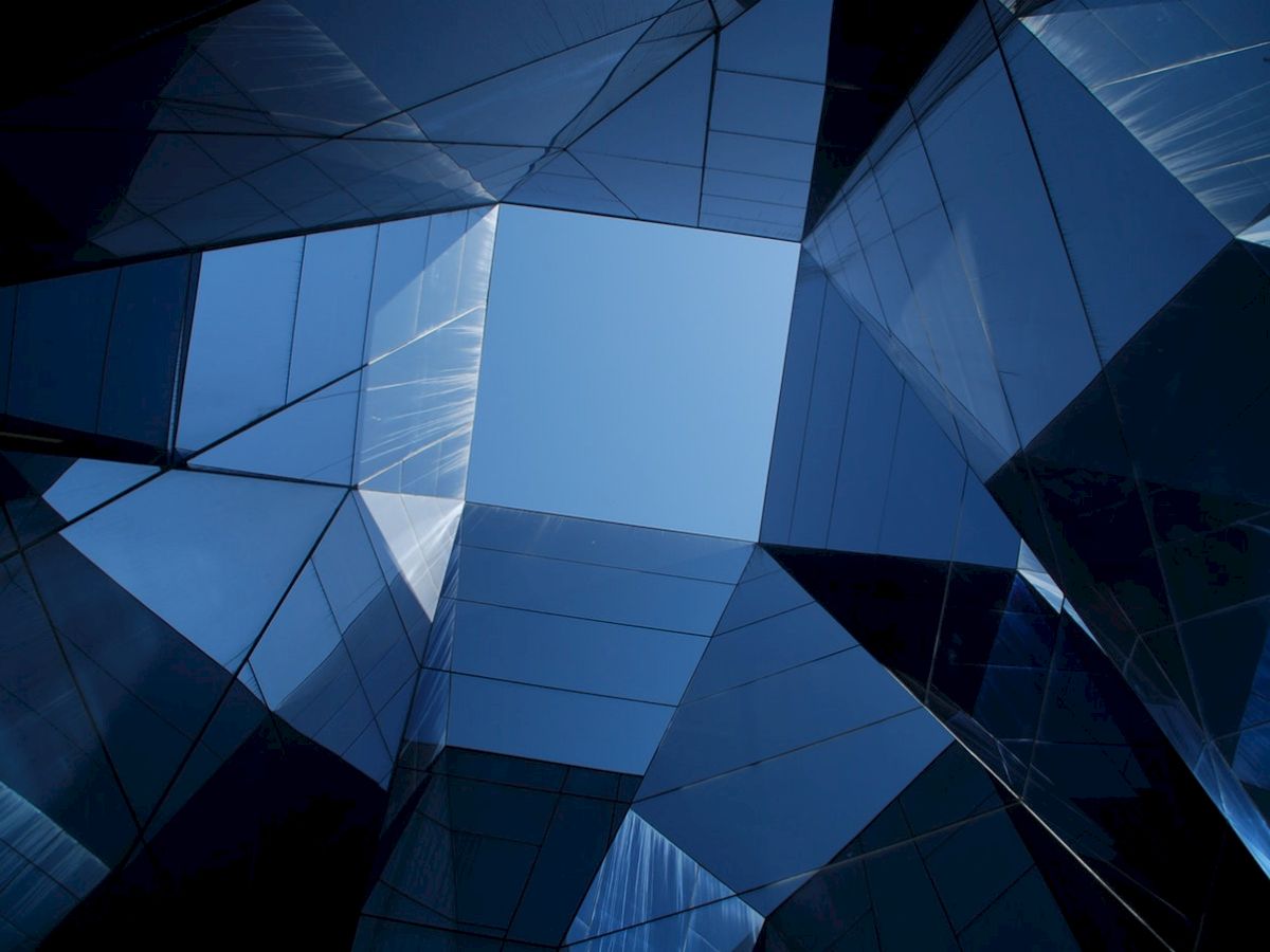 This image shows an abstract view of reflective glass structures forming a geometric pattern with a sky visible in the center.