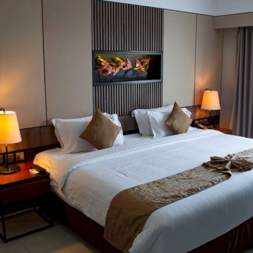 A neatly made hotel room bed with decorative pillows, side tables with lamps, and wall art above the headboard.