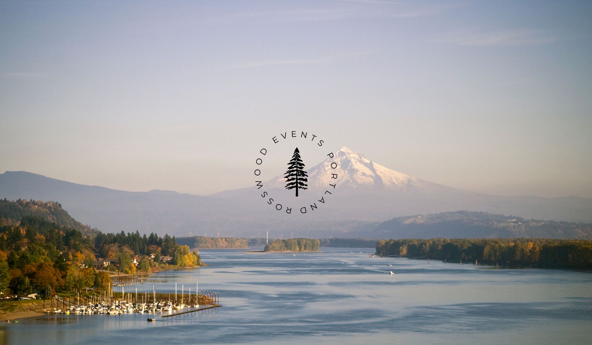 A serene landscape with a river, surrounding trees, mountains in the background, and a logo with a circular text and tree design in the center.