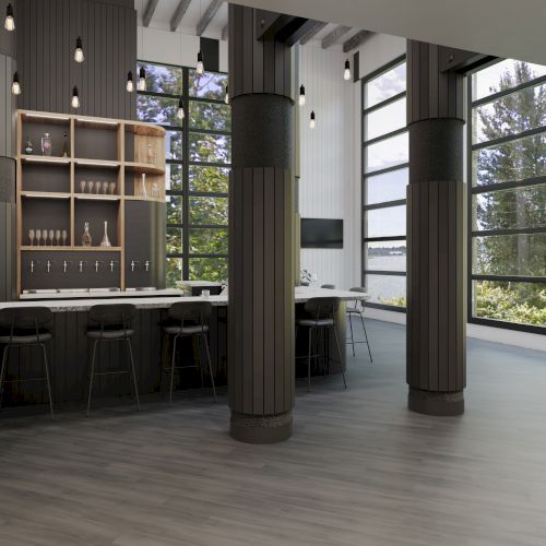 The image shows an empty modern bar area with high stools, columns, large windows, and a view of trees outside.