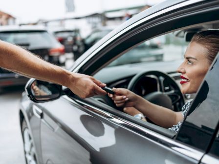 A person in a car receives a key from someone outside through the window, indicating a car handover or valet service.