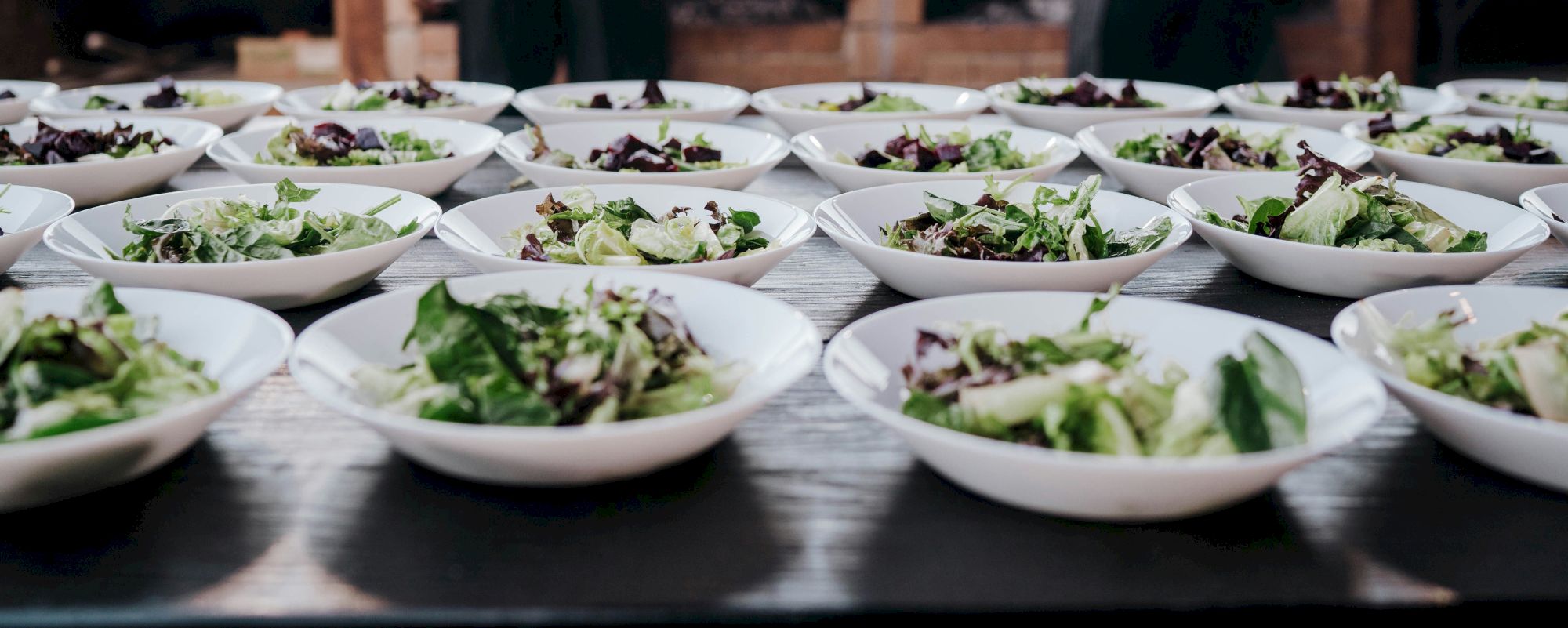 The image shows multiple plates of mixed green salads arranged in rows on a table, ready to be served.