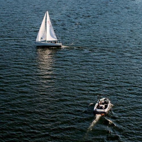 A sailboat and a motorboat are on a vast expanse of water, navigating separately across the deep blue surface.