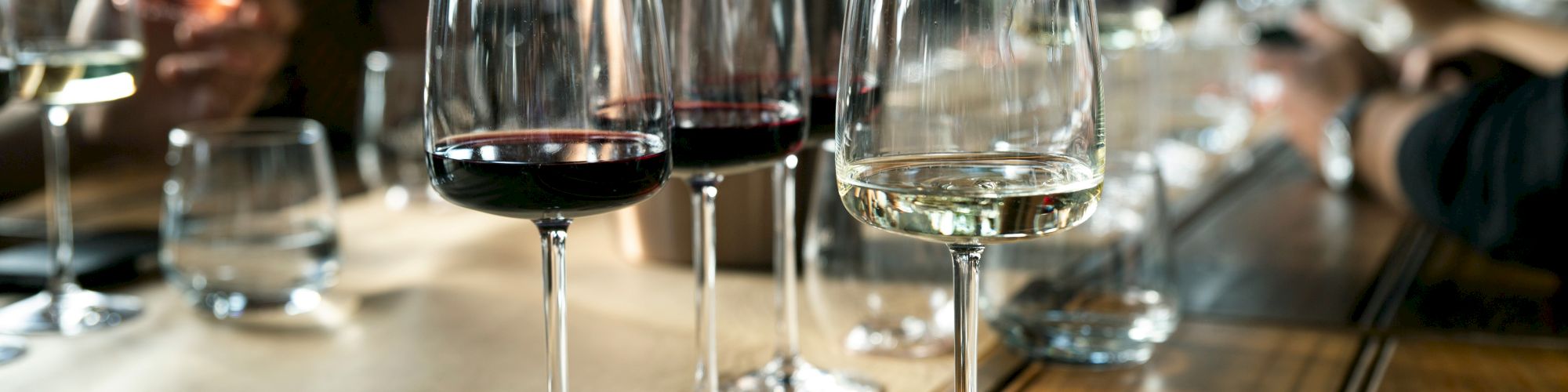 A table with multiple wine glasses, some filled with red wine and others with white, set for a gathering or tasting event.