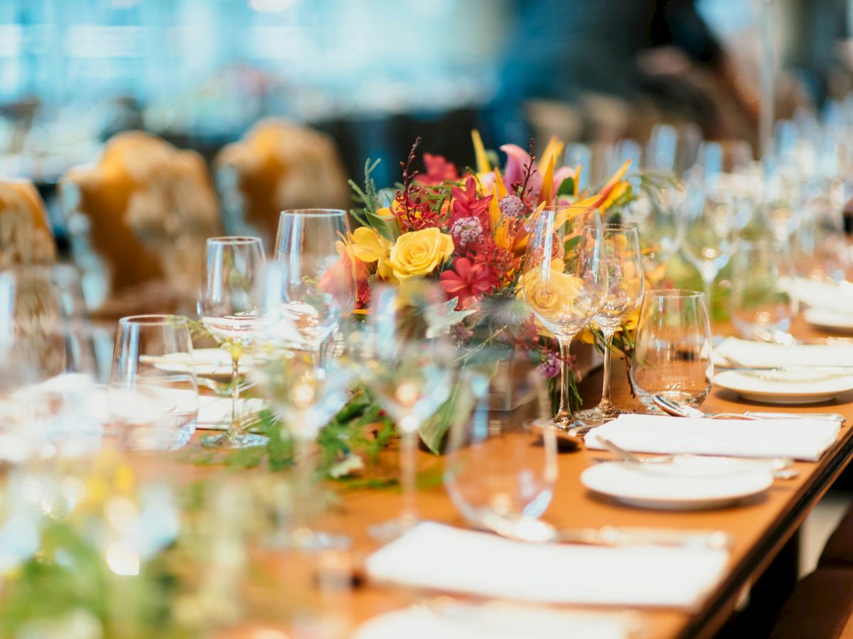A beautifully set dining table features elegant glassware, colorful floral centerpieces, and neatly arranged plates and napkins.