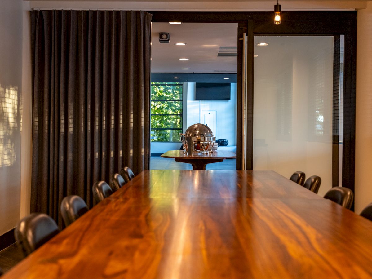 A long wooden conference table with black chairs, a doorway at the far end, and soft ambient lighting in a modern meeting room.