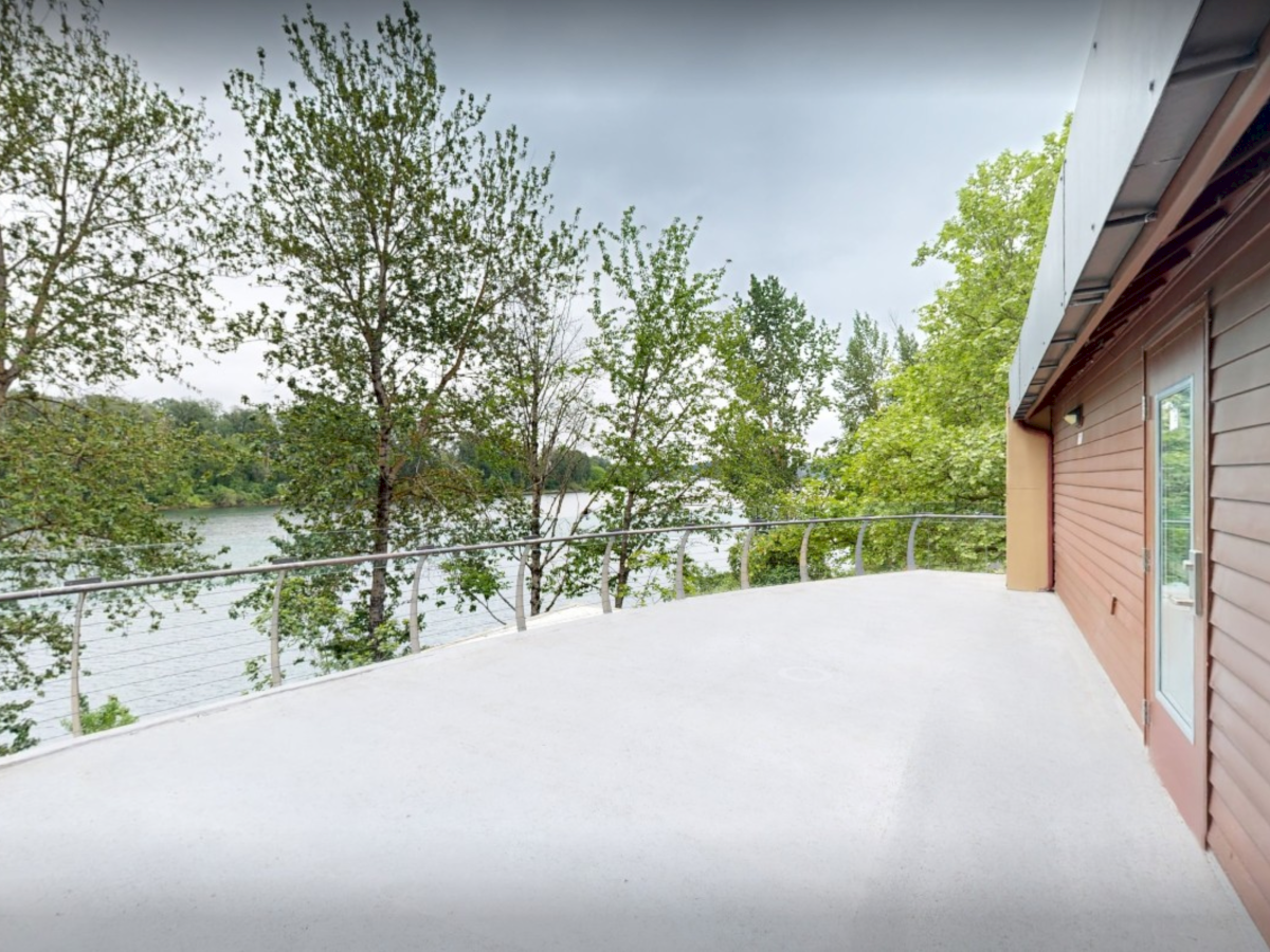 Balcony beside a house overlooking a calm lake with green trees and a cloudy sky.