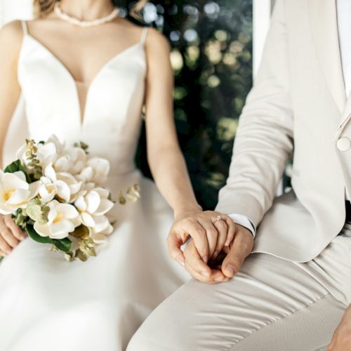 A wedding couple holding hands; the bride holds a bouquet, both in formal attire.