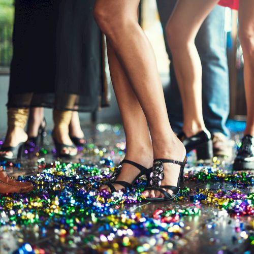 People dancing on a floor covered in colorful confetti, showing various footwear, at a lively party or celebration scene.