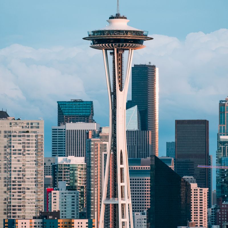 This image shows the Space Needle in Seattle with city skyscrapers in the background under a cloudy sky.