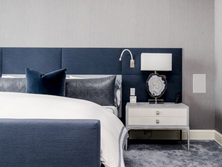 A modern bedroom with a blue and white color scheme features a bed, pillows, a nightstand with a lamp, and decorative accents.