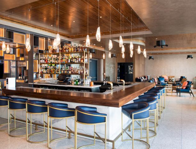 A modern bar with blue stools, a central bar counter, and stylish pendant lights, creating a cozy and inviting atmosphere.