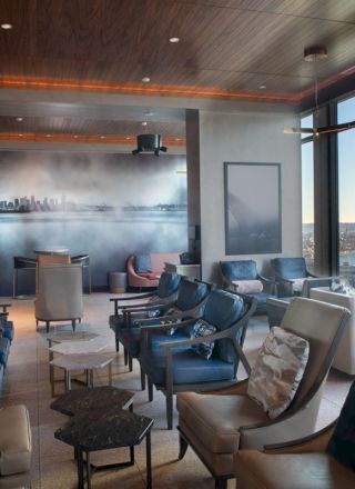 The image shows a modern, elegant lounge with chairs, cushioned seating, and large windows offering a scenic view.