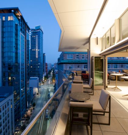A modern rooftop terrace with seating, overlooking a city street lined with tall buildings during the evening.