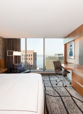 A modern hotel room with a large bed, wall-mounted TV, desk, and a window overlooking the city.