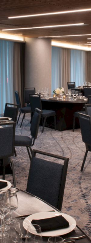 A banquet hall set with round tables, black chairs, white plates, black napkins, and floral centerpieces, ready for an event.