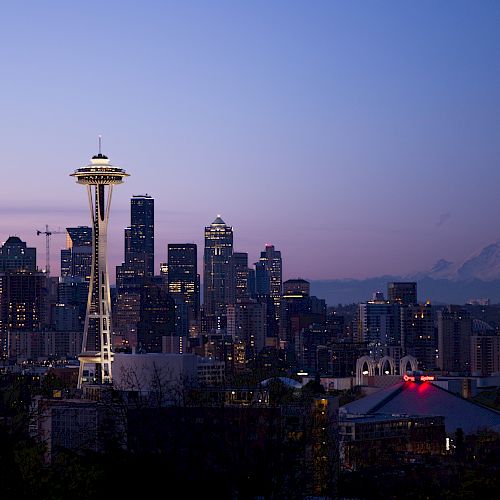 The image shows a city skyline at dusk with a prominent needle-like tower and a mountain in the background.
