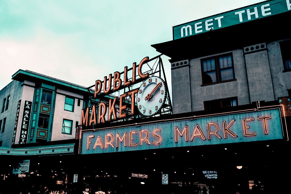 The image shows a neon sign reading "Public Market" and "Farmers Market," with a clock, part of a market area.