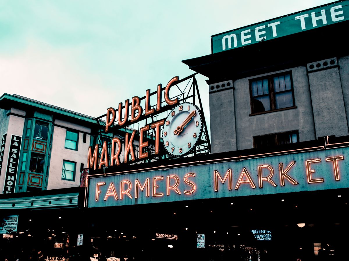 The image shows a neon sign reading "Public Market" and "Farmers Market," with a clock, part of a market area.