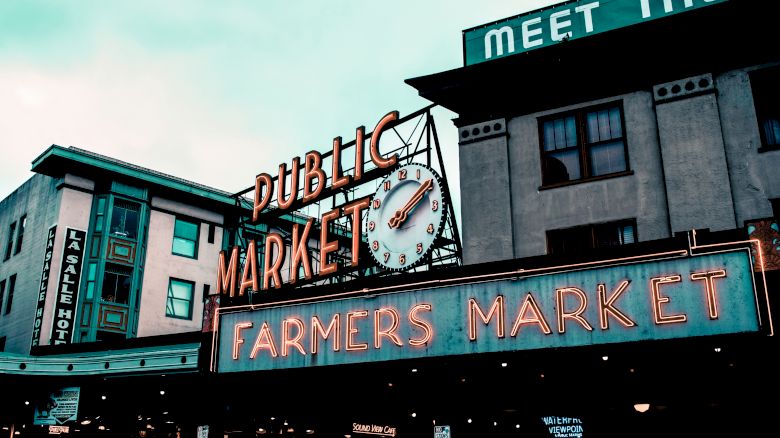 The image shows a neon sign reading "Public Market" and "Farmers Market," with a clock, part of a market area.