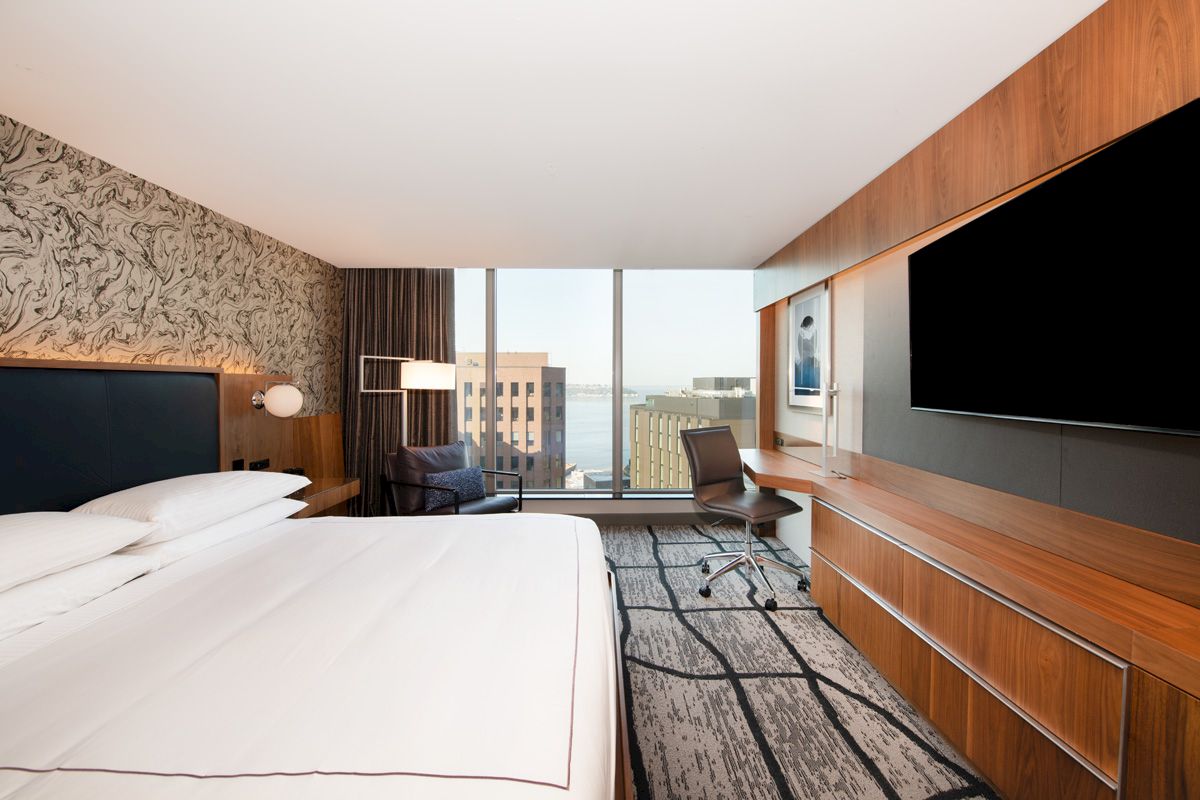 A modern hotel room featuring a large bed, a flat-screen TV, a work desk, and a window with a city view.