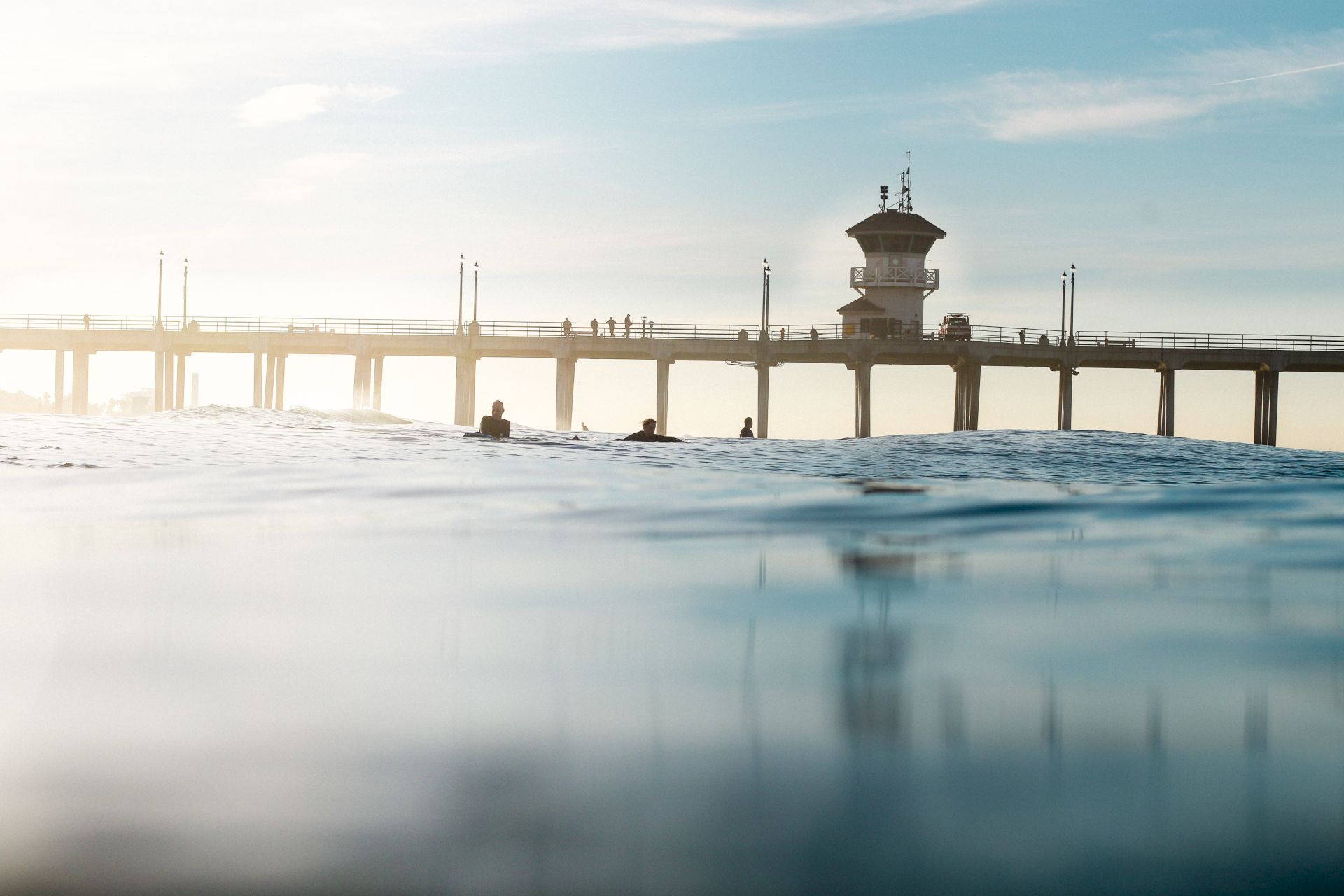 A view of a pier with a tower and people, captured from the water, under a clear blue sky.